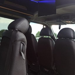 SOMAR MARCIN SOBCZAK - Wnętrze luksusowego busa do przewozu osób, widoczne czarne skórzane fotele z zagłówkami, oświetlenie LED na suficie i zamontowany telewizor.