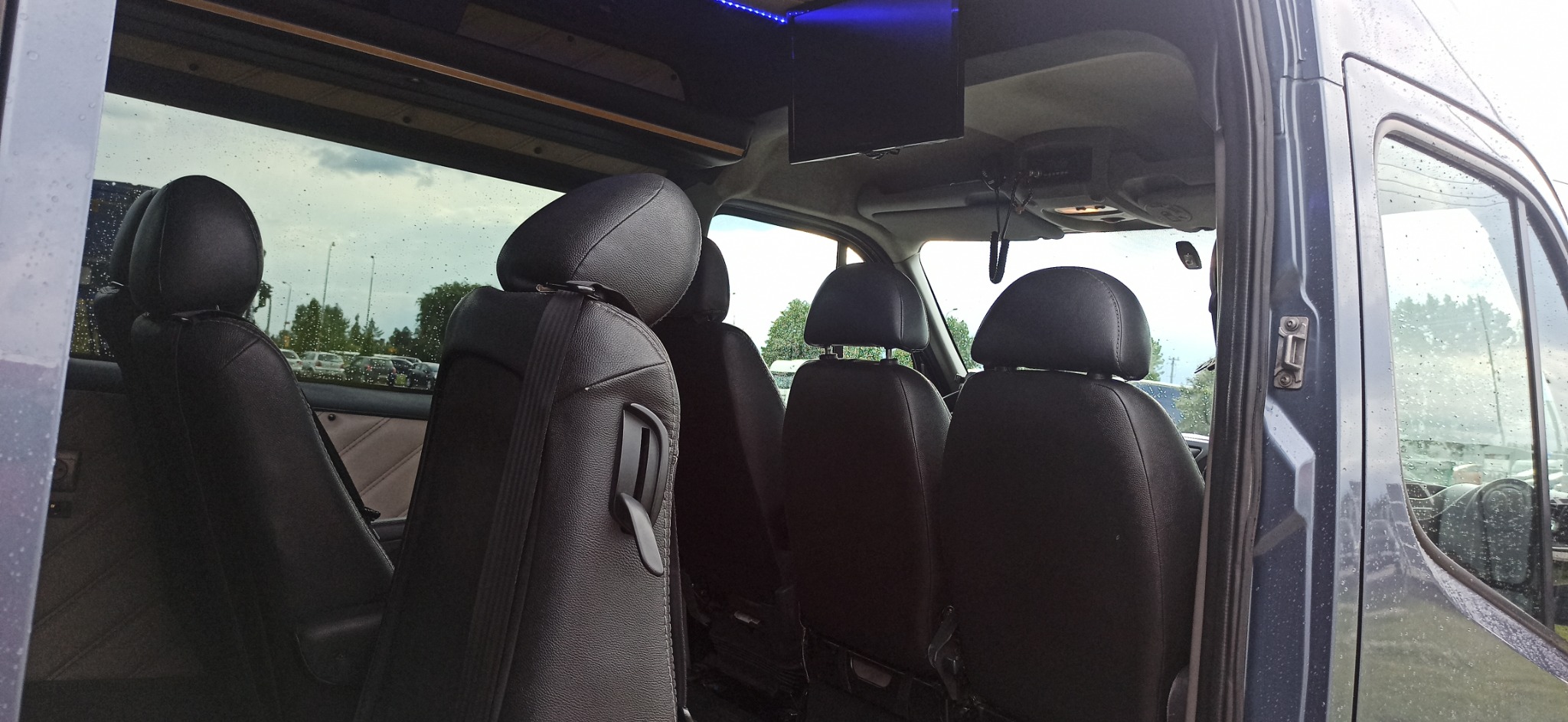 Wnętrze luksusowego busa do przewozu osób, widoczne czarne skórzane fotele z zagłówkami, oświetlenie LED na suficie i zamontowany telewizor.