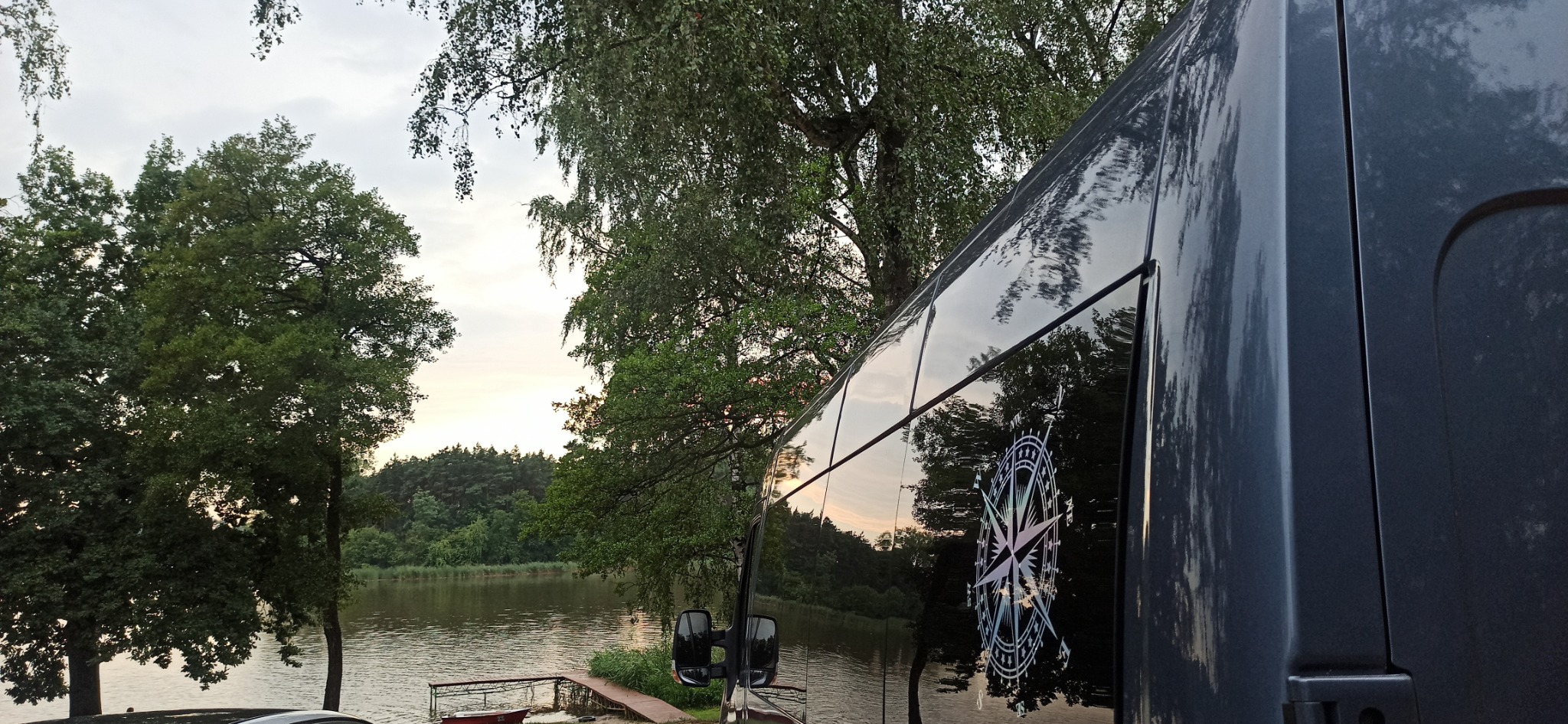 Boczny widok czarnego busa z kompasem na tle jeziora i drzew o zmierzchu.