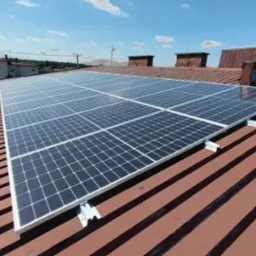 Panel fotowoltaiczny zamontowany na brązowym, blaszanym dachu domu jednorodzinnego, widok z góry przy słonecznej pogodzie.