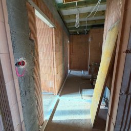 EKa Instalacje - Wnętrze w trakcie budowy z widocznymi pustakami ceramicznymi, instalacją elektryczną w ścianie i elementami konstrukcji sufitu. Widoczne przewody i metalowe profile podłogowe.