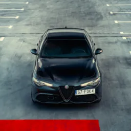 Czarna Alfa Romeo Giulia zaparkowana na szarym parkingu, widok z góry na przód samochodu, widoczna tablica rejestracyjna i czerwona linia na dole kadru.