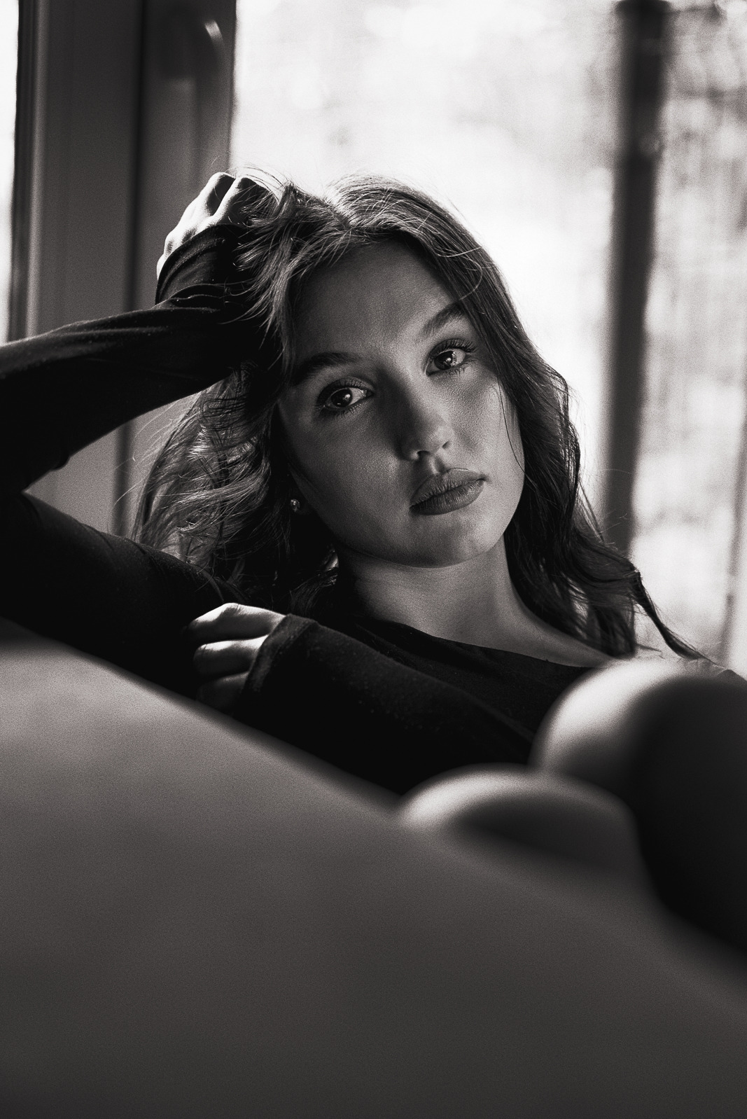 Portret młodej kobiety w czerni, opierającej głowę na ręce, z melancholijnym spojrzeniem w obiektyw, w czarno-białej tonacji.