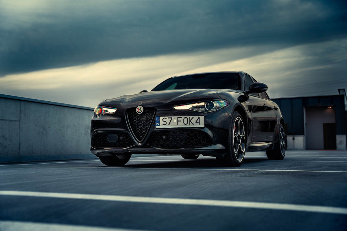 Czarna Alfa Romeo Giulia na parkingu, widok z przodu, pochmurne niebo w tle.