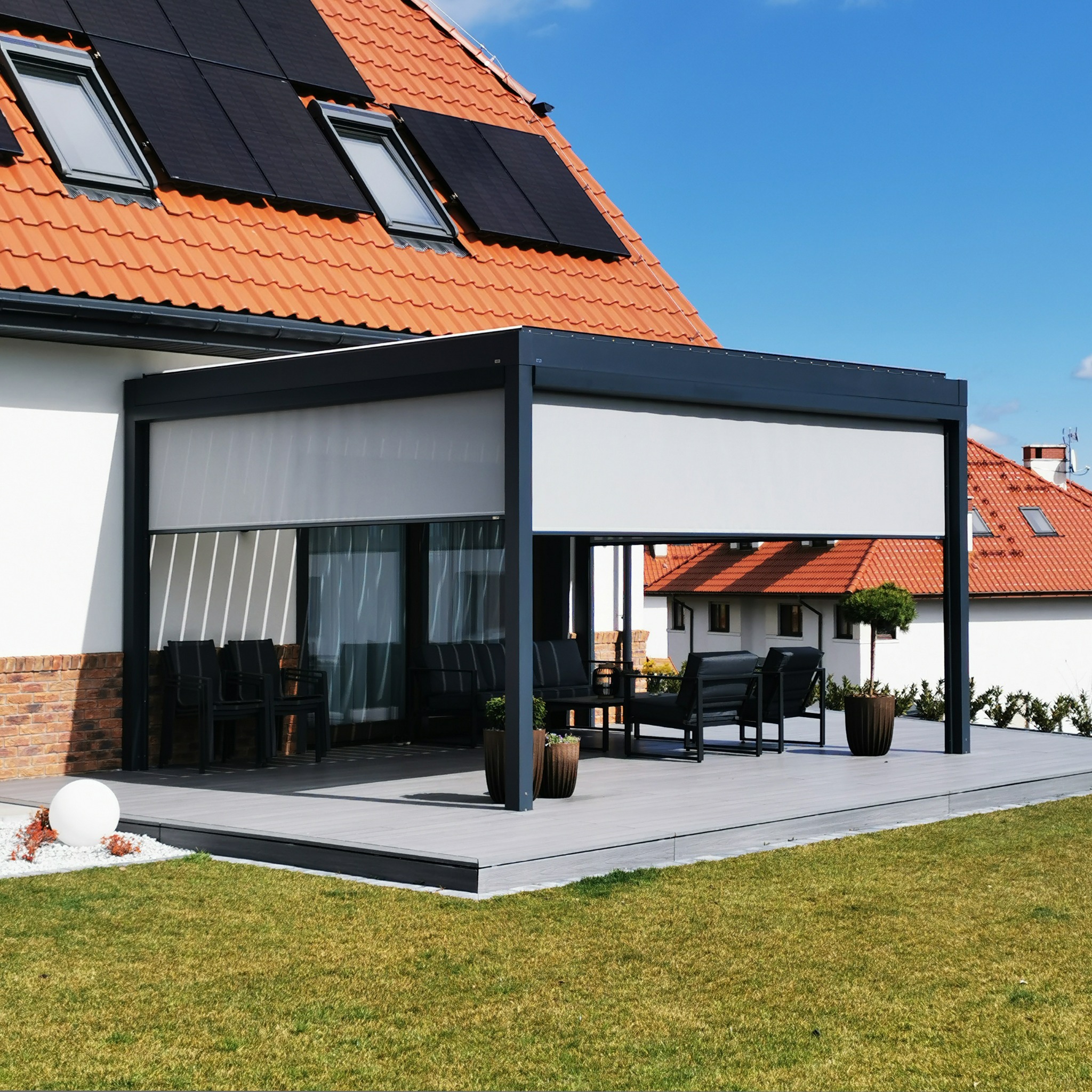 Nowoczesna pergola bioklimatyczna z zasłonami typu Zip Screen, tworząca komfortową przestrzeń na tarasie w Kołbaskowie, z widocznymi panelami słonecznymi na dachu domu.