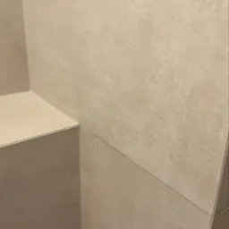 Fragment wykończonej łazienki w Brynek: beżowe, matowe płytki ceramiczne ułożone na ścianie i zabudowie, widoczne wąskie fugi.