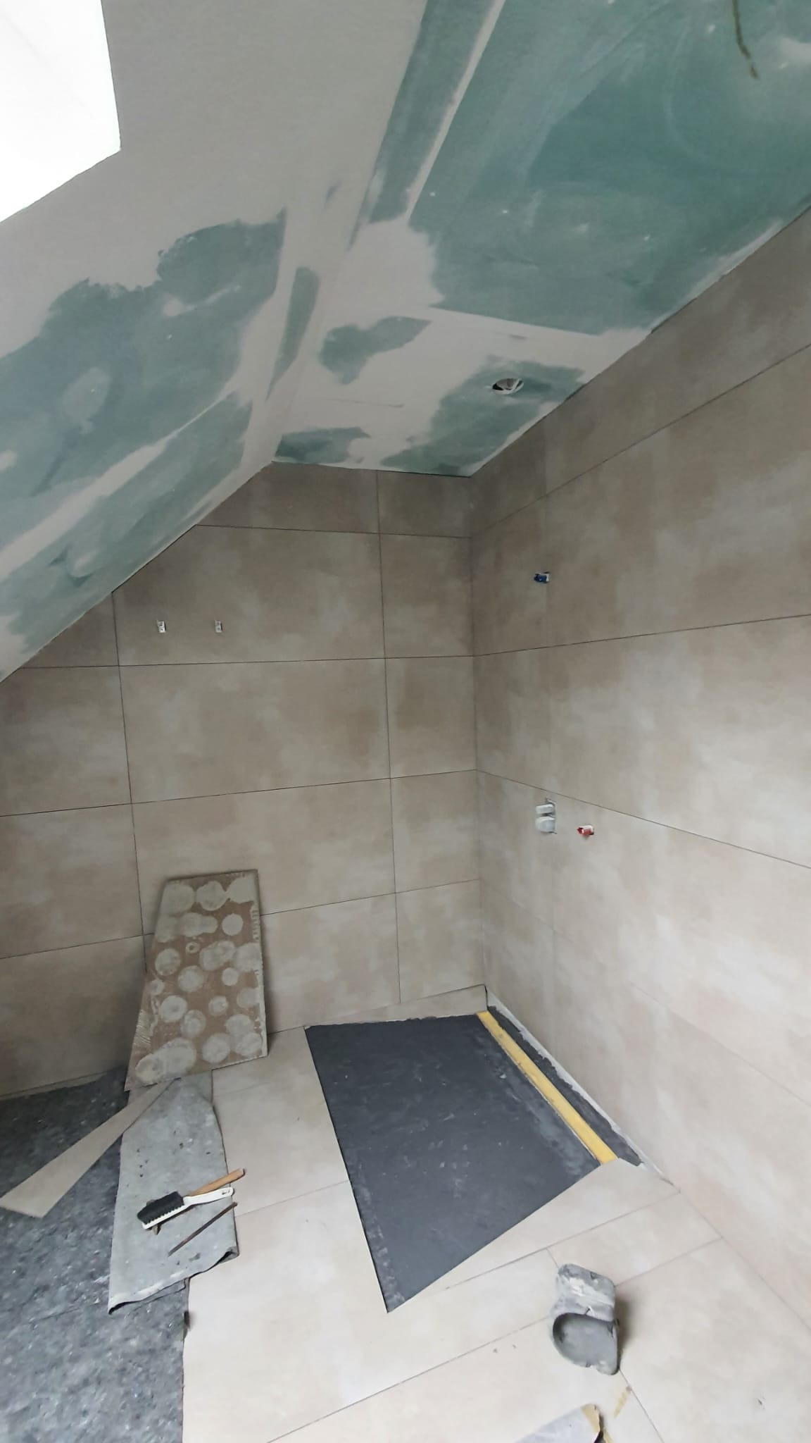 Łazienka na poddaszu w trakcie remontu: ułożone beżowe płytki ścienne, przygotowane podłoże pod prysznic z widoczną hydroizolacją, sufit z płyt gipsowo-kartonowych w trakcie szpachlowania...