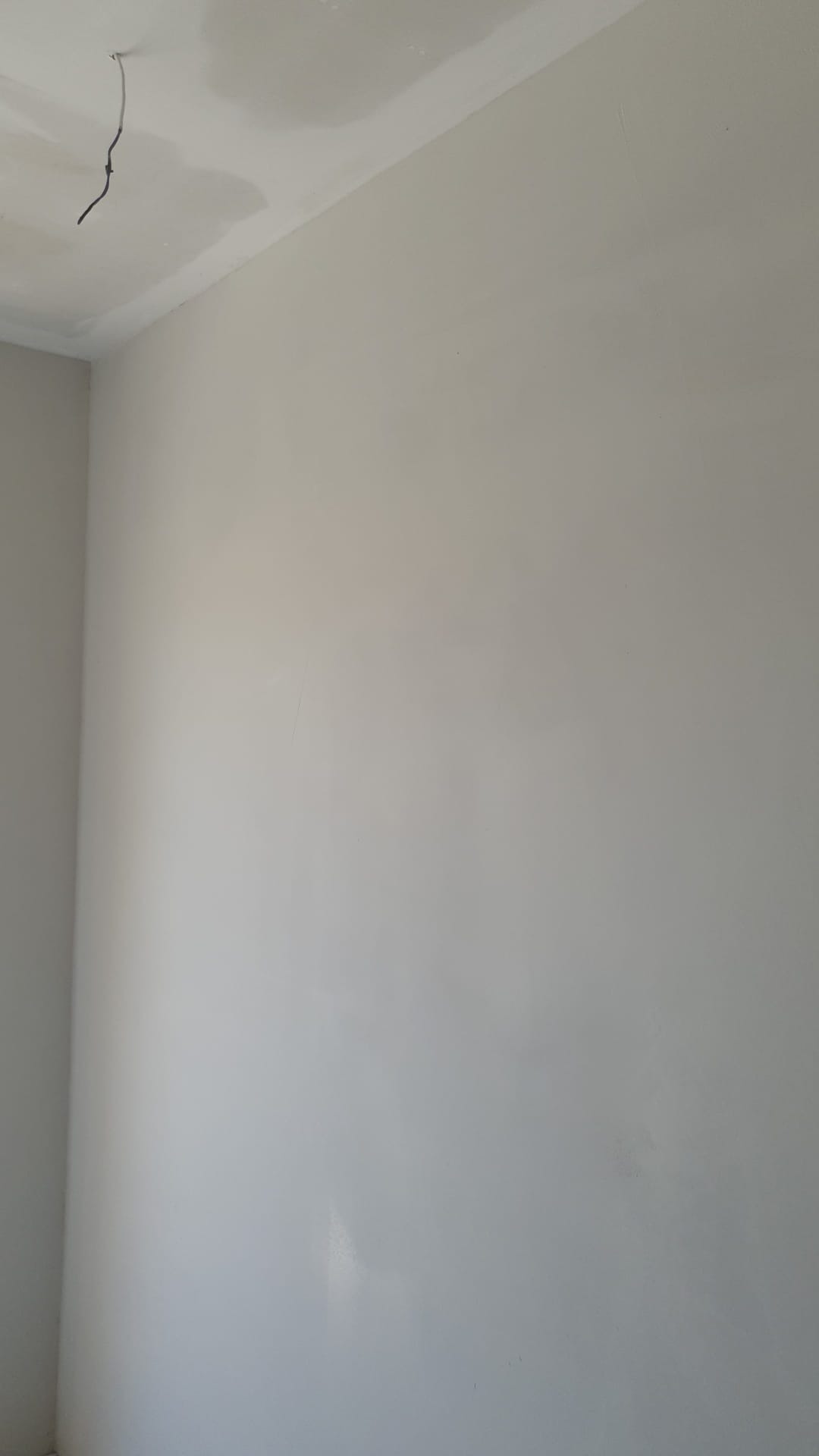Świeżo położona gładź na ścianie i suficie w rogu pokoju, widoczne wystające kable elektryczne.