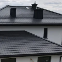 Nowoczesny dom jednorodzinny z ciemnoszarą dachówką płaską Erlus Linea, widoczne kominy i rynny w kolorze dachu.