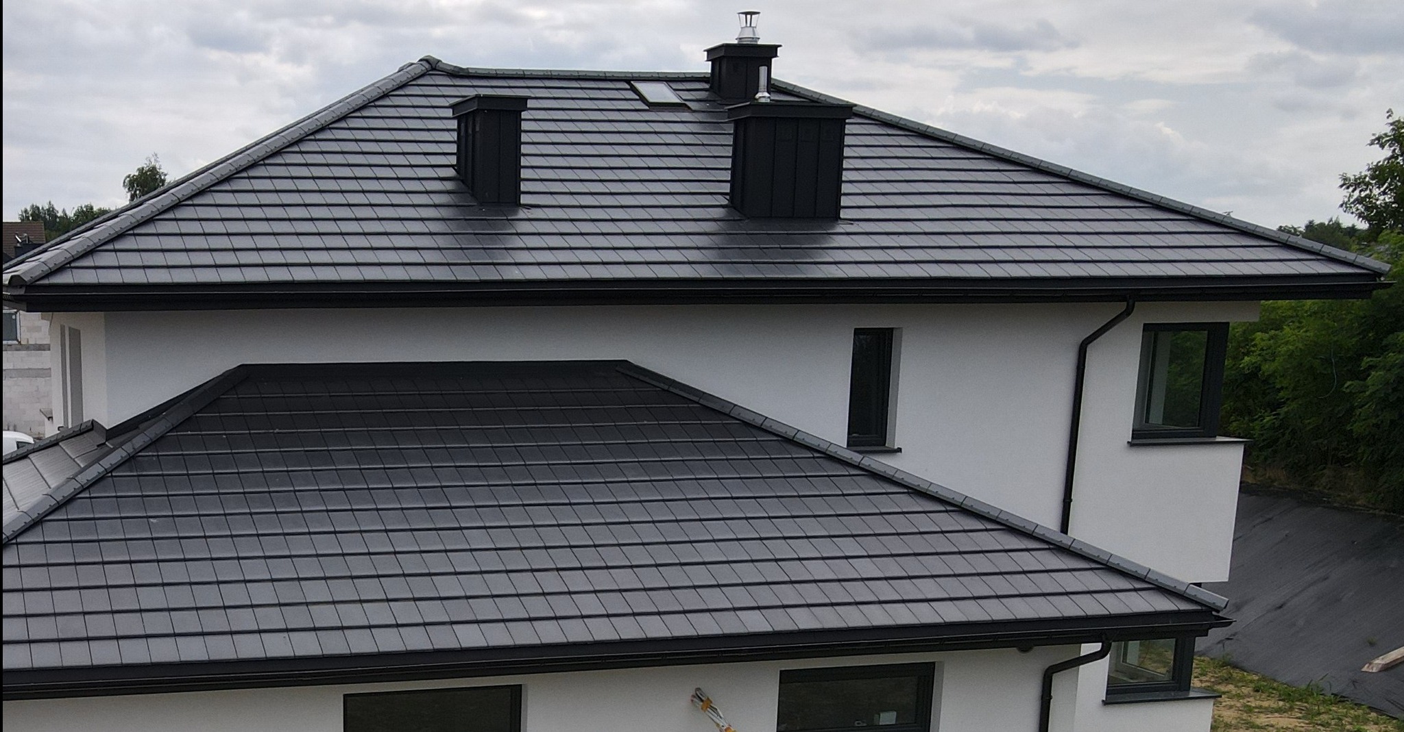 Nowoczesny dom jednorodzinny z ciemnoszarą dachówką płaską Erlus Linea, widoczne kominy i rynny w kolorze dachu.