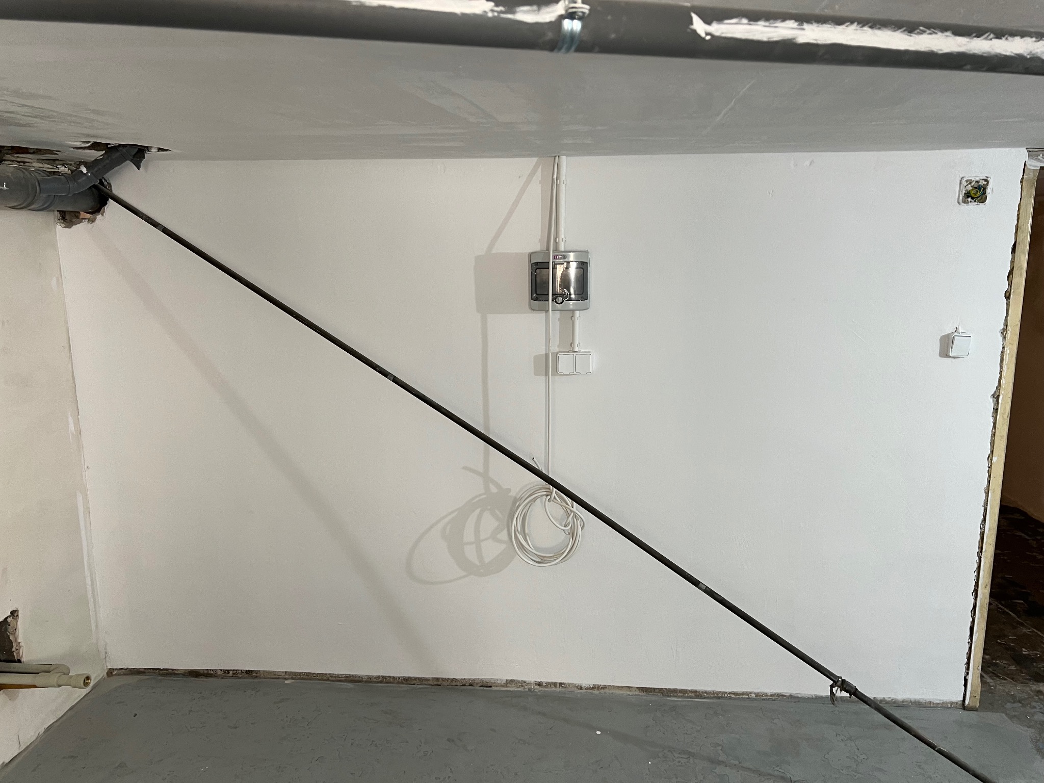 Świeżo wyszpachlowana ściana z widocznymi przewodami elektrycznymi, rurami i elementami instalacji, podparta metalową rozpórką.