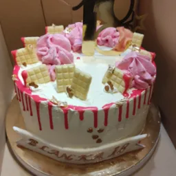 Tort urodzinowy z białym kremem, różowymi bezami, dekoracjami z białej czekolady i złotymi akcentami, przygotowany w Warszawie na osiemnaste urodziny.