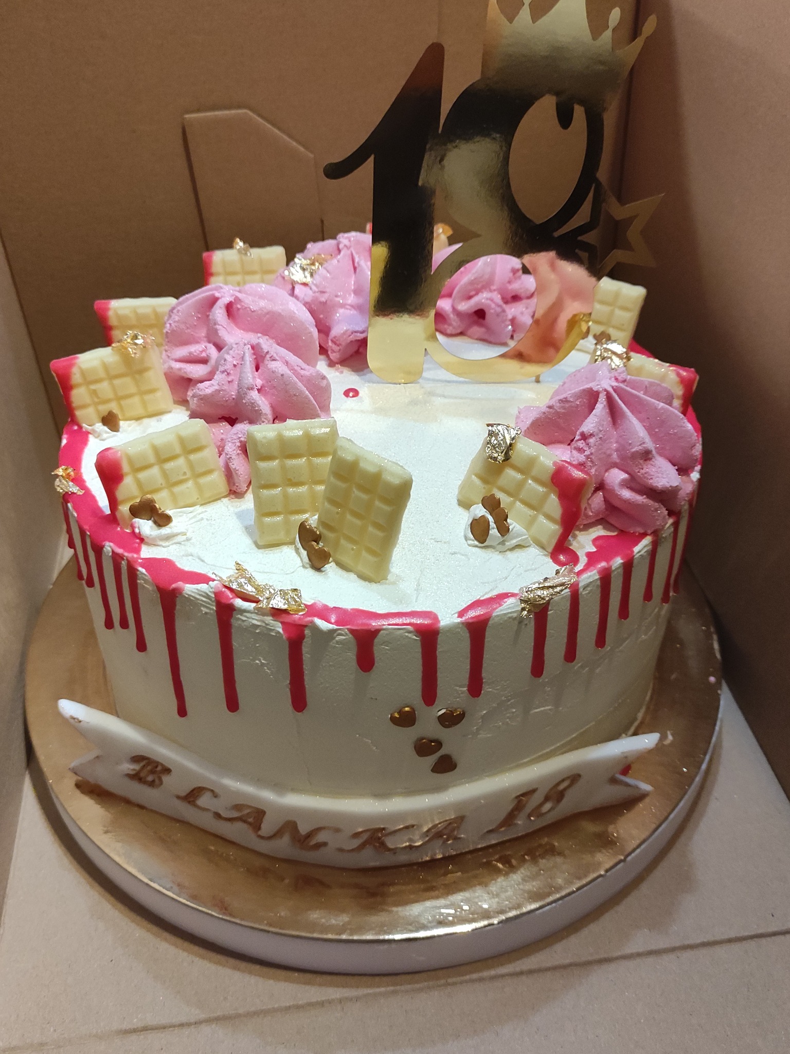 Tort urodzinowy z białym kremem, różowymi bezami, dekoracjami z białej czekolady i złotymi akcentami, przygotowany w Warszawie na osiemnaste urodziny.