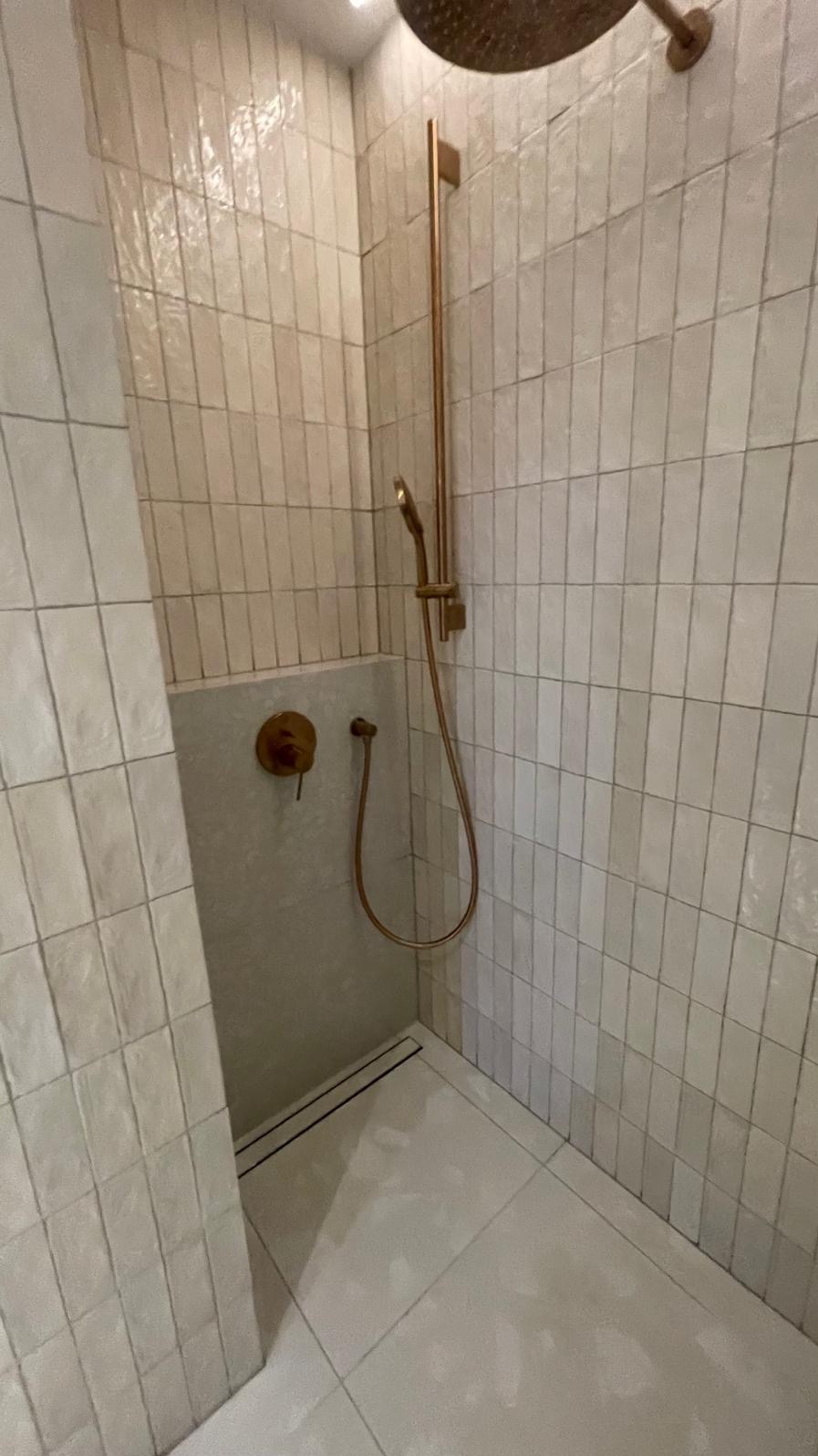 Wykończony prysznic w Sokołowie Podlaskim z beżowymi, pionowo ułożonymi płytkami, złotą armaturą i odpływem liniowym.