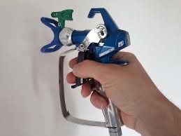 Pistolet natryskowy do malowania w dłoni, zbliżenie na dyszę i spust, widoczna niepomalowana ściana w tle.