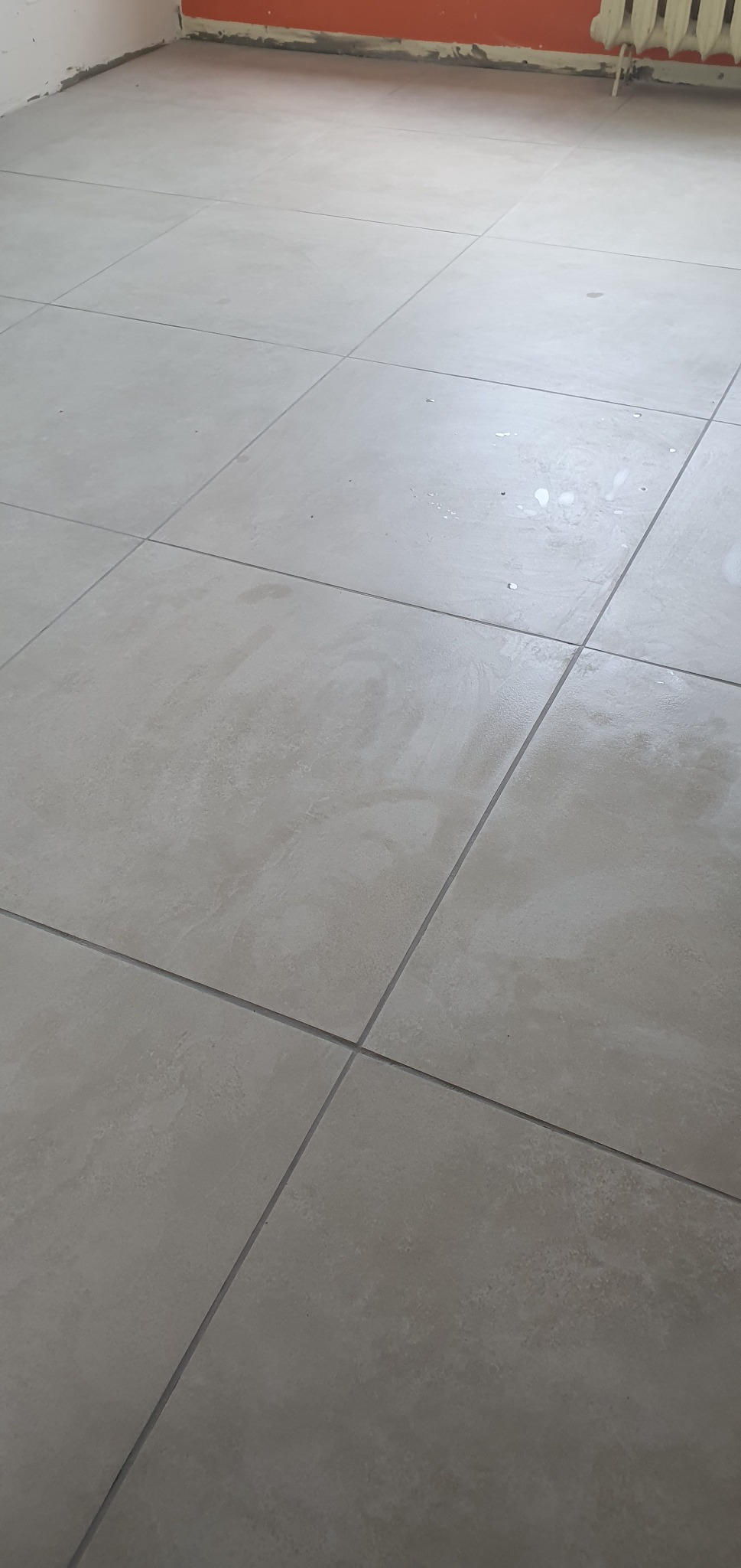 Świeżo położone, jasnoszare płytki podłogowe z ciemnoszarą fugą, widoczne ślady po pracach wykończeniowych.