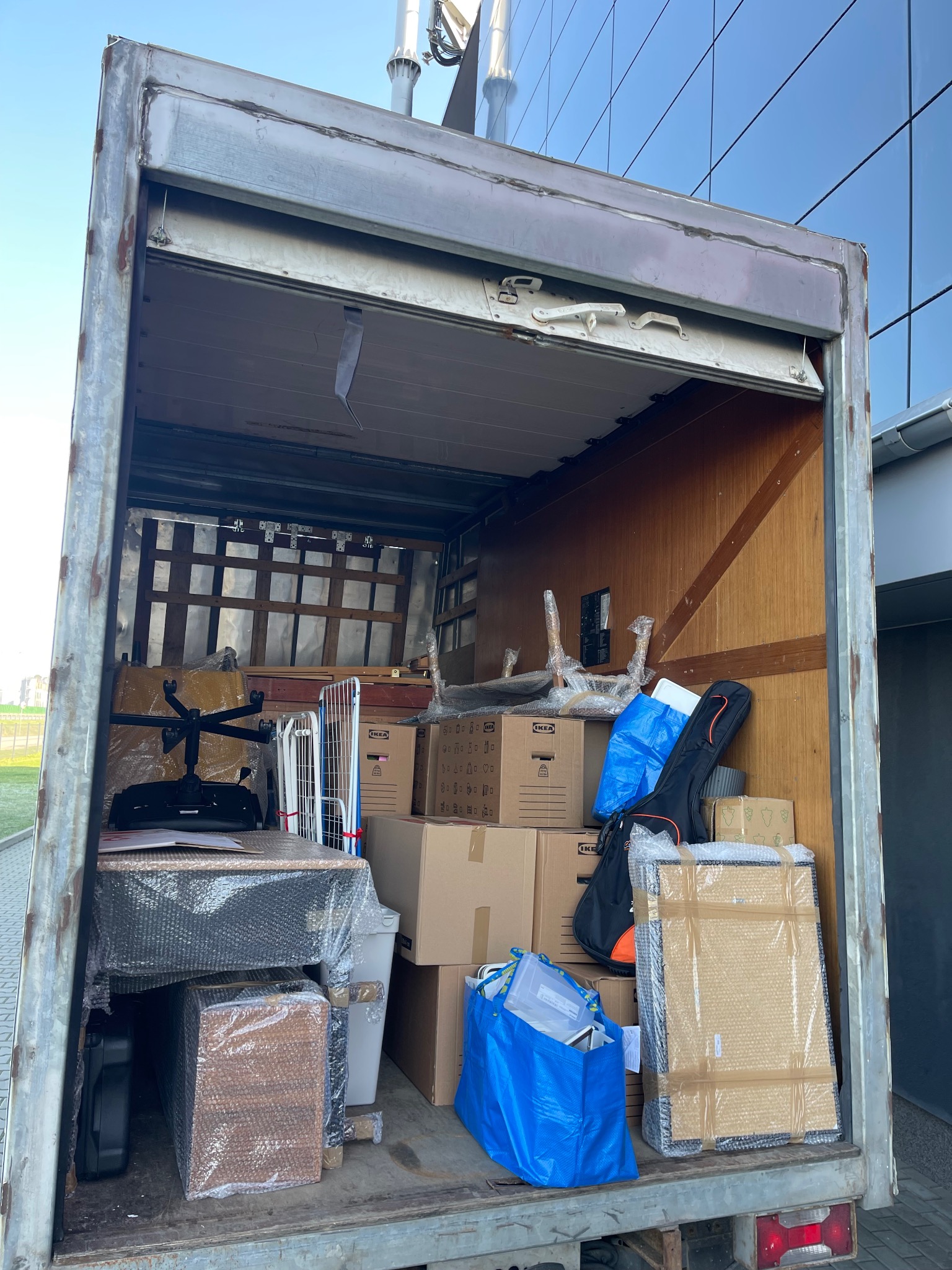Wnętrze paki busa załadowane meblami, biurkiem, krzesłem obrotowym i kartonami marki IKEA, zabezpieczonymi folią bąbelkową, gotowe do transportu.