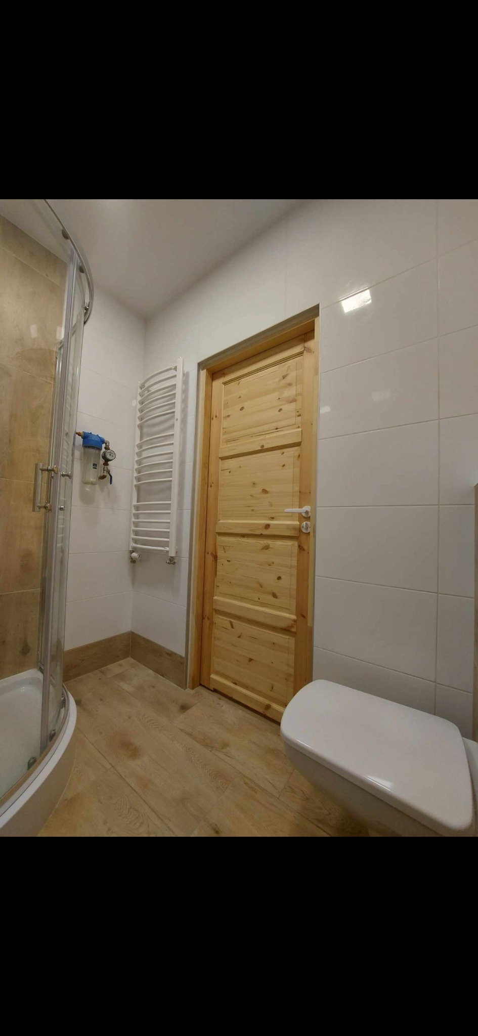 Jasna łazienka po remoncie z kabiną prysznicową, grzejnikiem drabinkowym, drewnianymi drzwiami i toaletą.