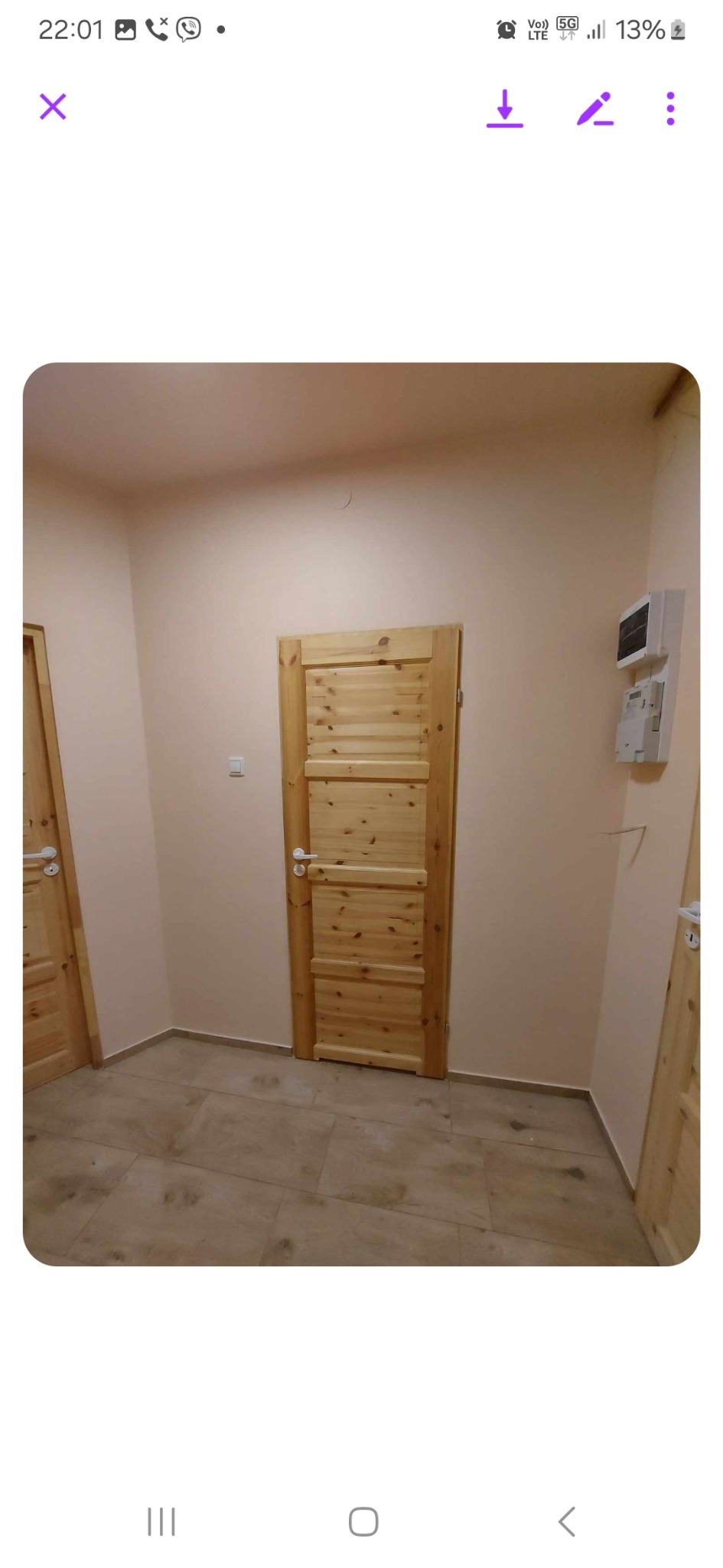 Wnętrze z dwiema drewnianymi, surowymi drzwiami z poziomymi panelami, jasnymi ścianami i podłogą z płytek imitujących drewno.