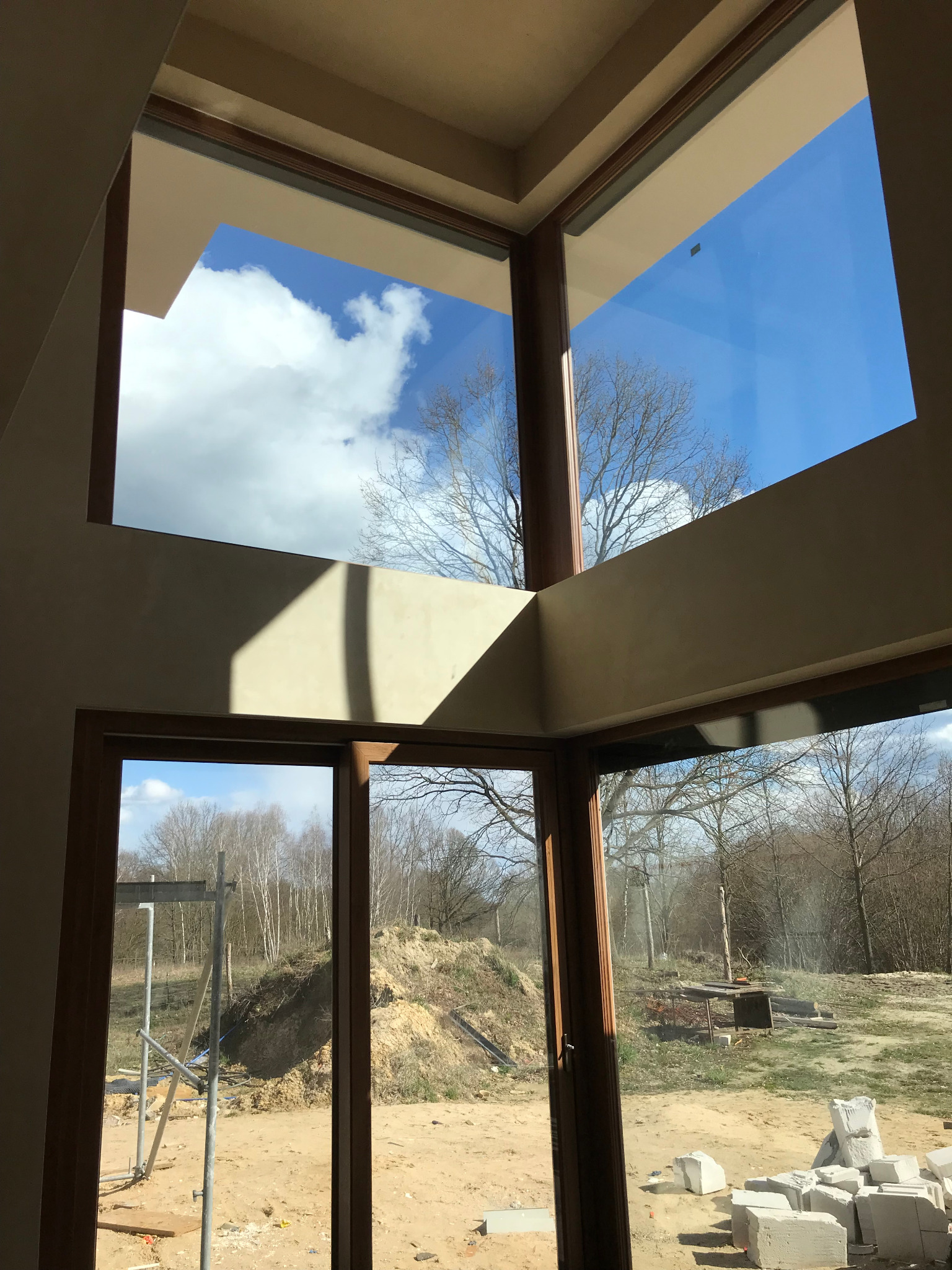 Wnętrze nowo wykończonego pokoju z widokiem na zewnątrz przez duże okna, ściany otynkowane na gładko, widoczne bloki budowlane i rusztowanie za oknem.