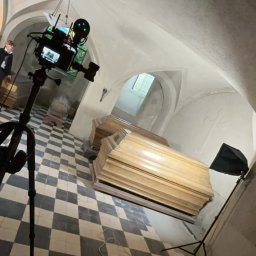 Aleksander Kwiecień - Fotografia - Krypta z kamerą na statywie rejestrującą ujęcie na trumny, oświetlenie studyjne i podłoga w szachownicę.