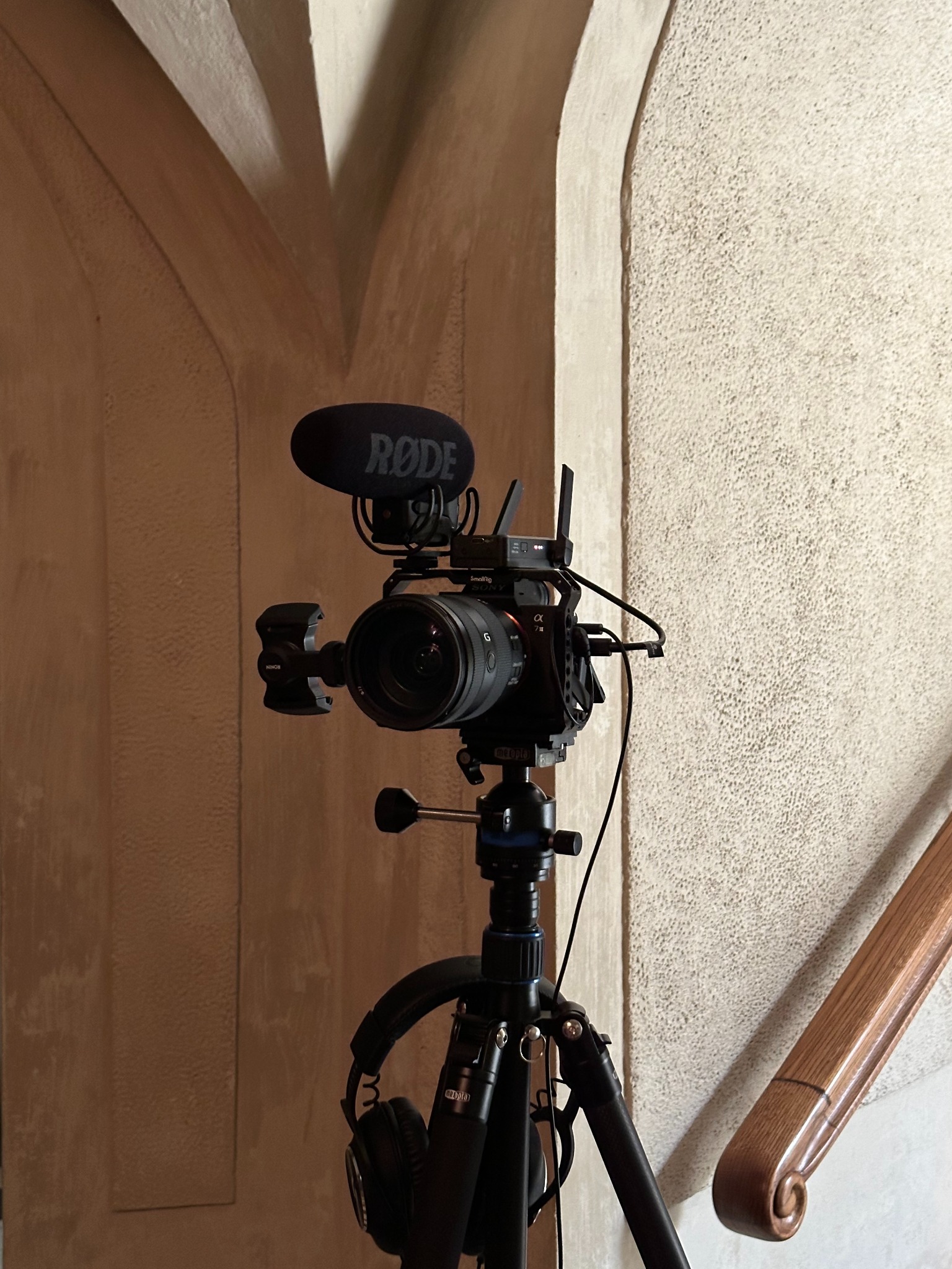 Profesjonalny aparat Sony z mikrofonem Rode na statywie, słuchawki zawieszone na statywie, tło stanowią architektoniczne elementy wnętrza.