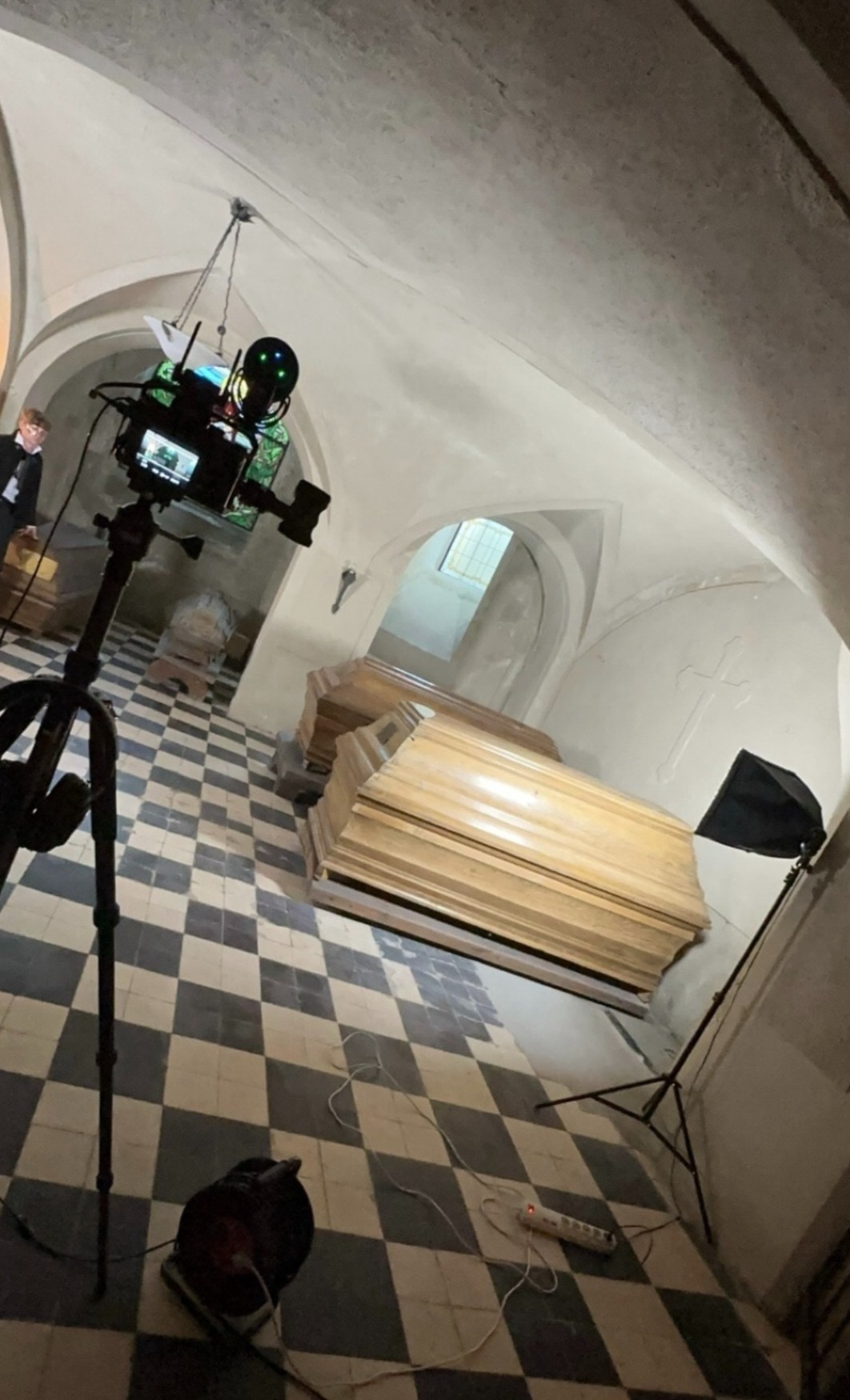 Krypta z kamerą na statywie rejestrującą ujęcie na trumny, oświetlenie studyjne i podłoga w szachownicę.