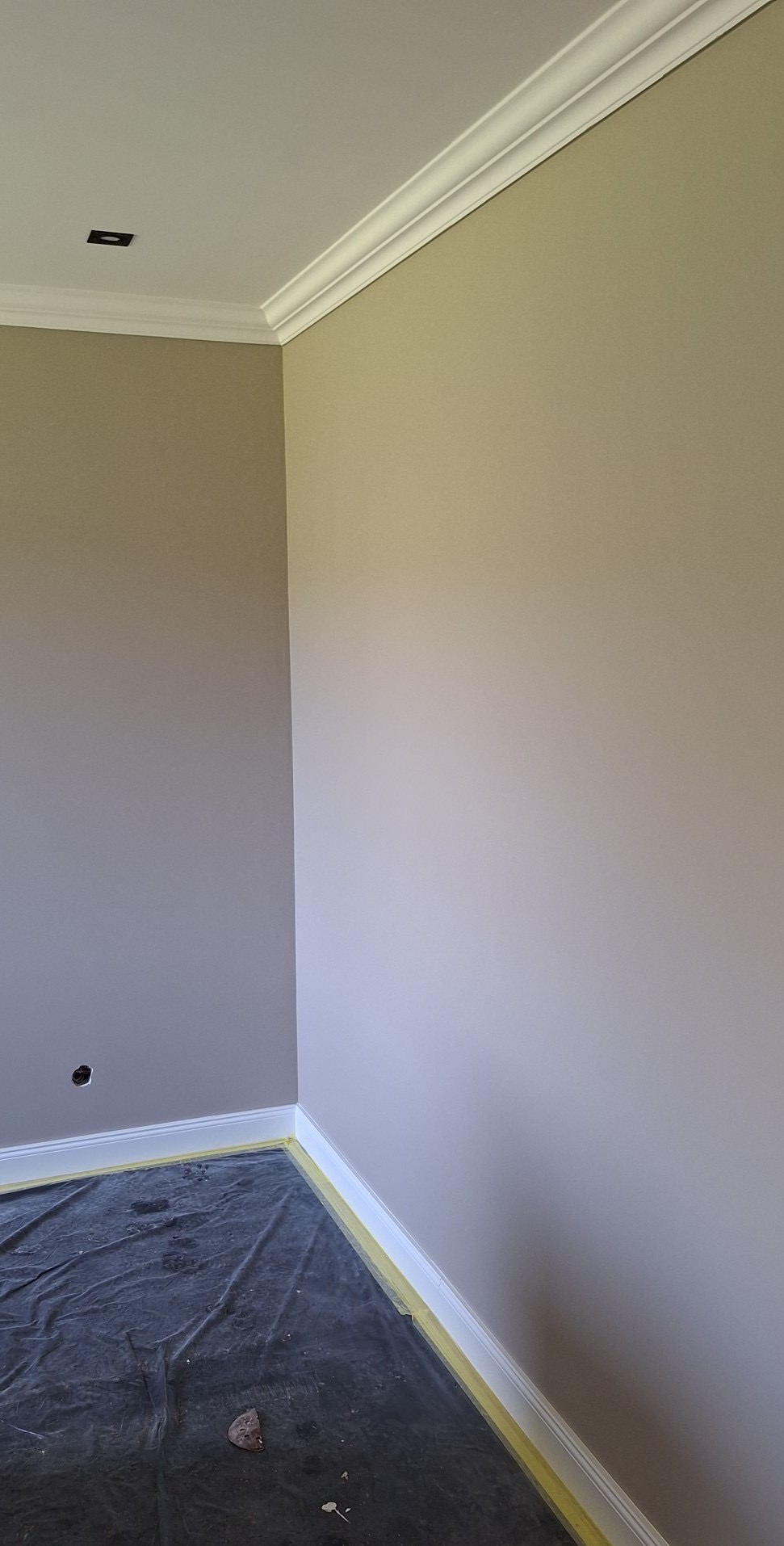 Pomieszczenie po świeżym pomalowaniu ścian w dwóch odcieniach szarości, z listwami przypodłogowymi i sufitowymi. Podłoga zabezpieczona folią malarską.