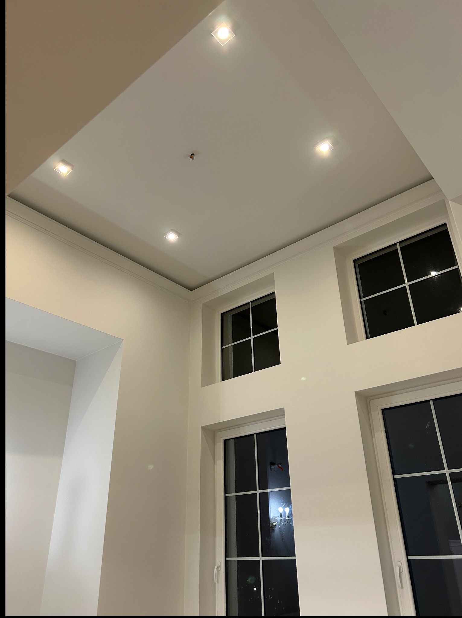 Białe ściany z trzema oknami i wbudowanymi lampami sufitowymi, widok z dołu, prezentujące wykończenie wnętrza w nowoczesnym stylu.