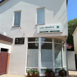 Fasada budynku z szyldem 'Luka Medica Przychodnia Medyczna Centrum Pomocy Psychologicznej', okna z żaluzjami i skrzynki z kwiatami.