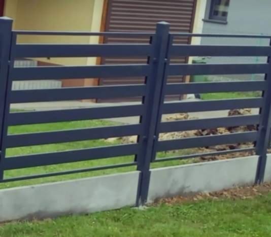 Nowoczesne, poziome przęsła w ciemnoszarym odcieniu, osadzone na betonowej podmurówce, tworzące ogrodzenie na tle budynku z brązową bramą garażową.