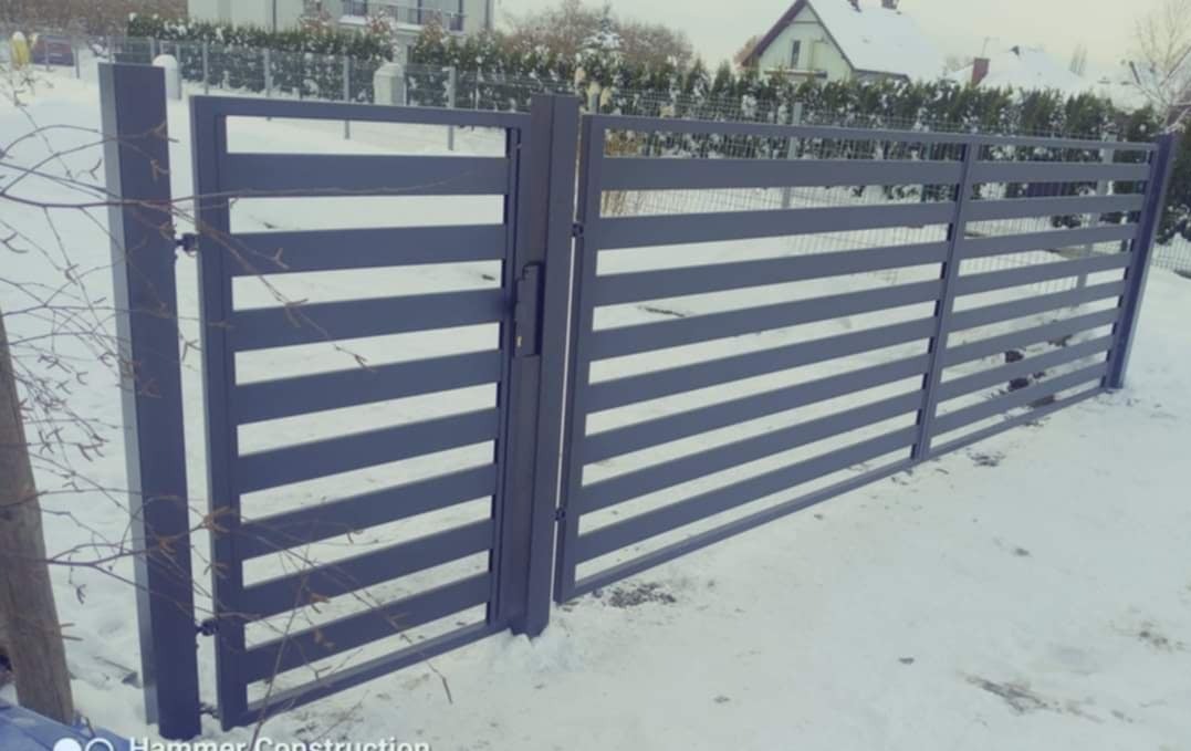 Nowoczesna, pozioma brama wjazdowa i przęsła w kolorze grafitowym, zamontowane w zimowym krajobrazie, z widocznym śniegiem i zabudową jednorodzinną w tle.