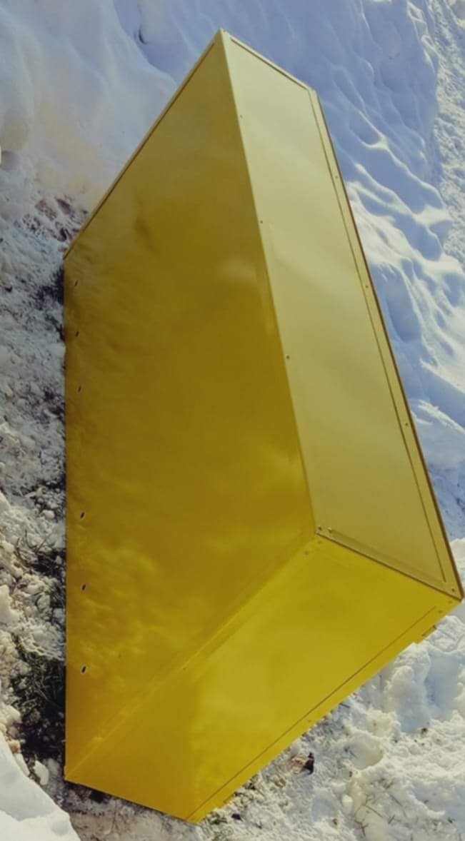 Żółta, metalowa skrzynia o trapezoidalnym przekroju, ustawiona na śniegu, widoczne nity i łączenia blach