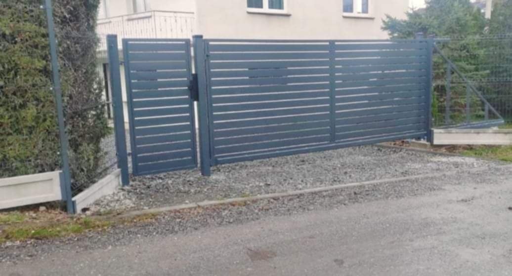 Nowoczesna, przesuwna brama wjazdowa z poziomymi panelami w kolorze szarym, na tle domu i zieleni.