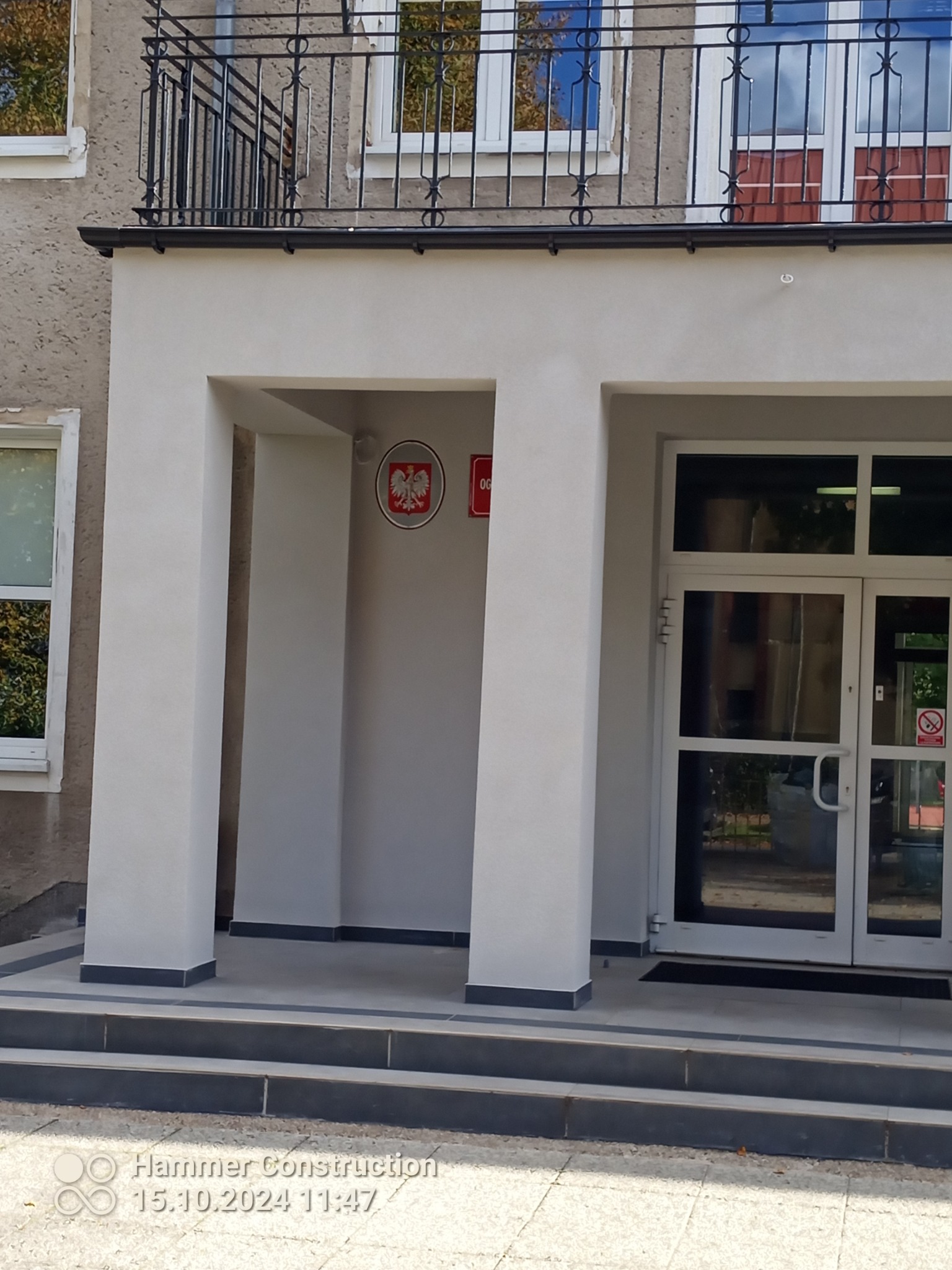 Odnowiona elewacja budynku publicznego z nowymi, jasnymi tynkami, widoczne wejście z kolumnami i godło państwowe.