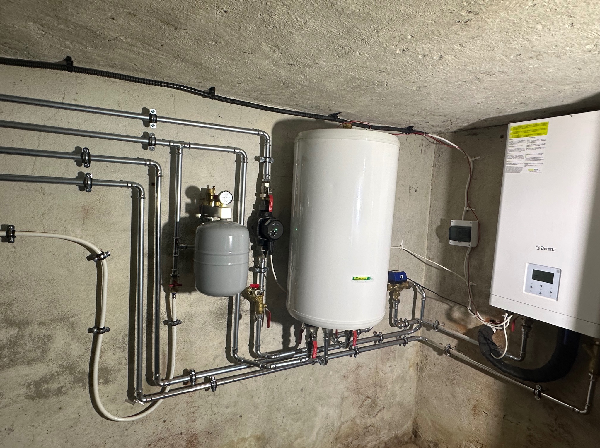 Kompletna instalacja grzewcza w piwnicy z widocznym zbiornikiem buforowym, pompą obiegową, kotłem gazowym Beretta i rurami ze stali nierdzewnej.