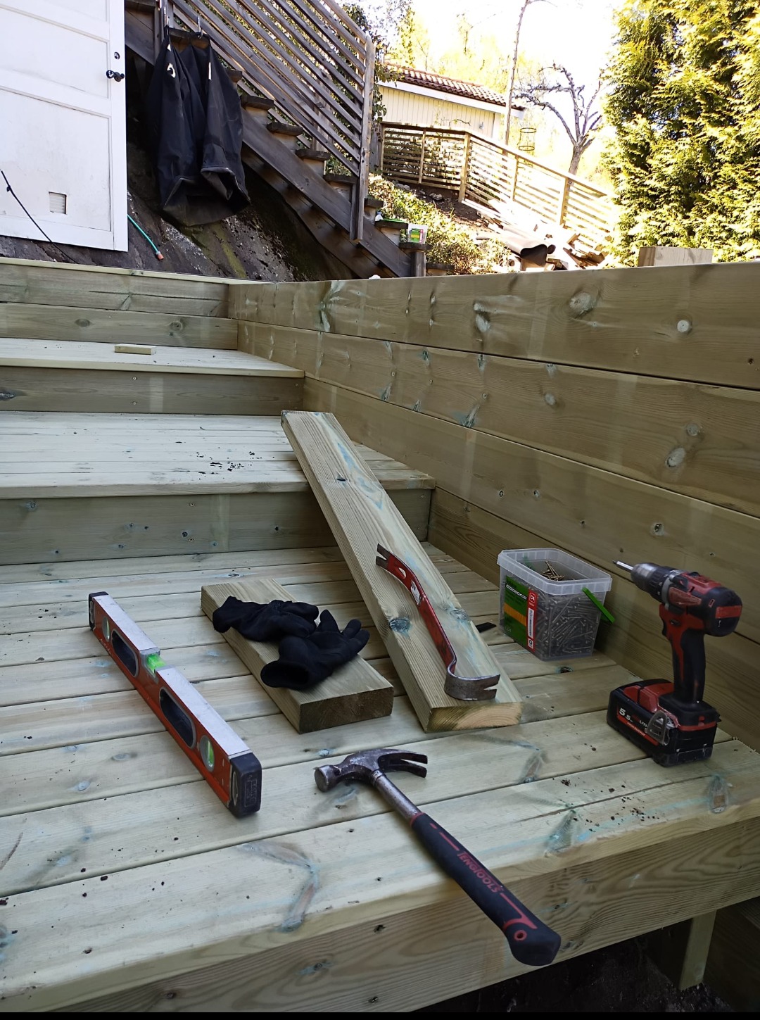 Budowa drewnianego tarasu schodkowego w ogrodzie: poziomica, młotek, wkrętarka i inne narzędzia na tle surowego drewna.
