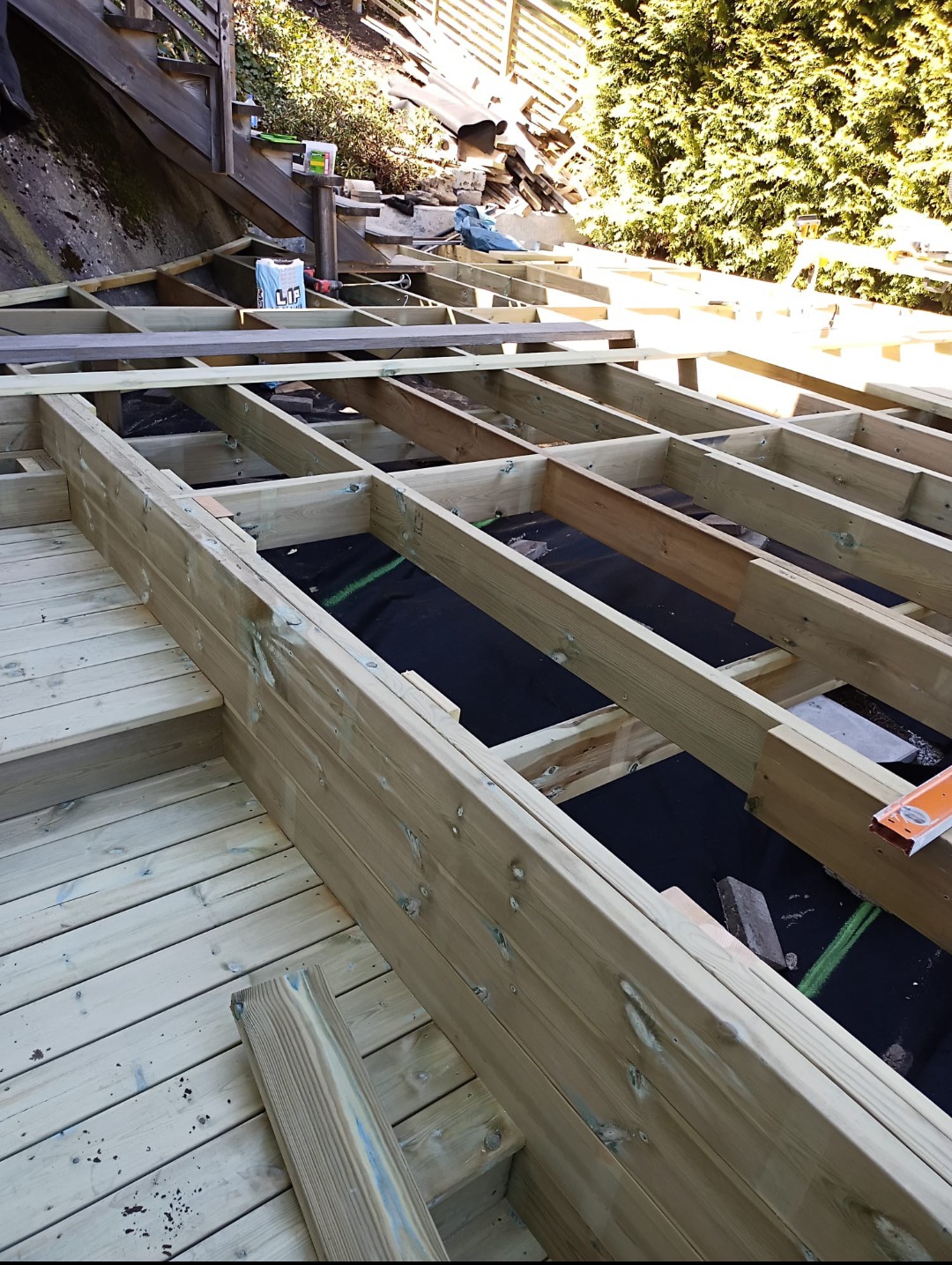 Konstrukcja drewnianego tarasu w trakcie budowy w Gdańsku, widoczne legary i podkład z czarnej membrany, w tle zielona roślinność.