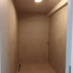 Wykończona łazienka z beżowymi płytkami na ścianach i podłodze, widoczny odpływ liniowy, przygotowane punkty pod armaturę, oświetlenie sufitowe.