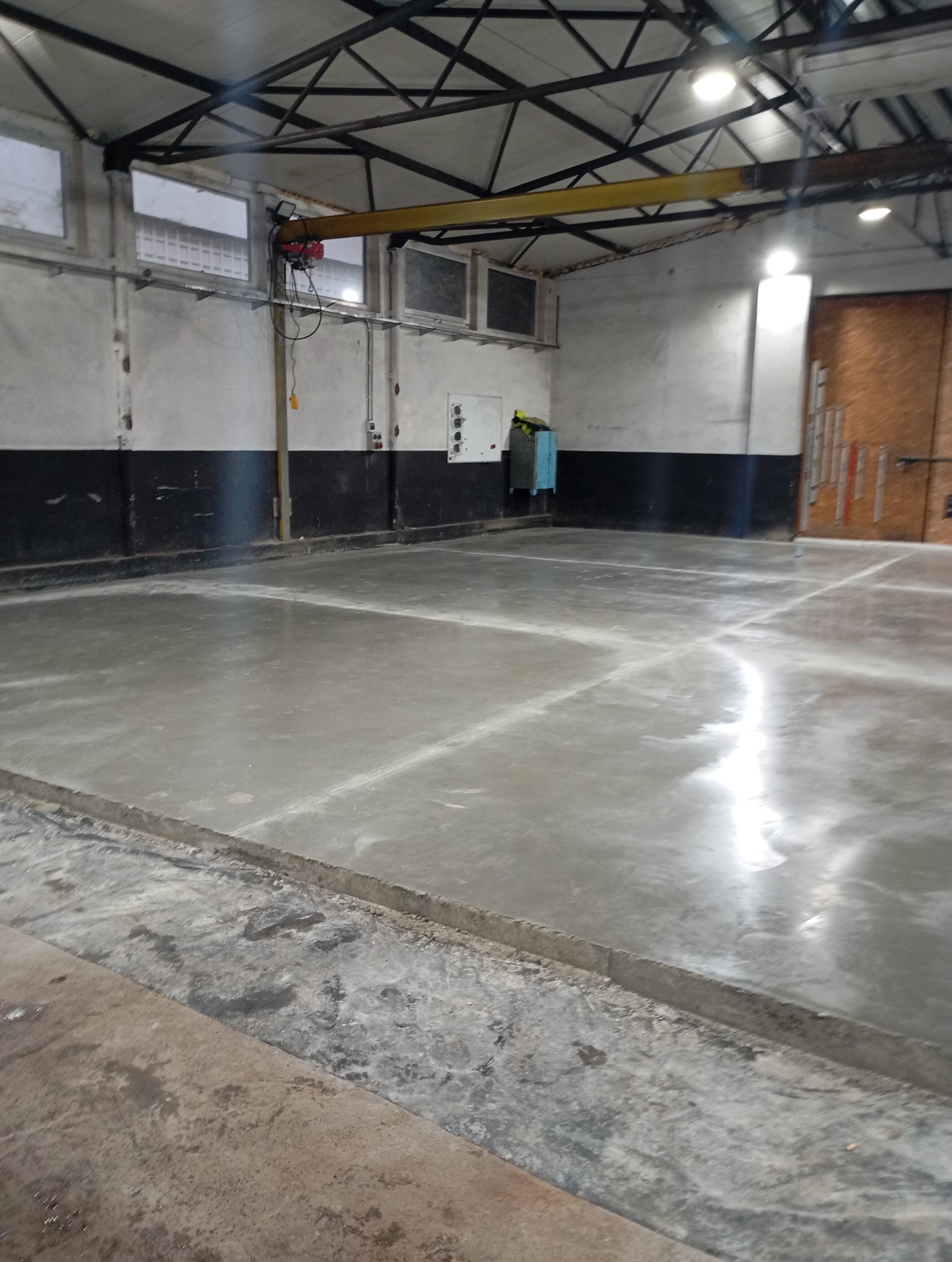 Świeżo wylana, gładka posadzka przemysłowa w hali z suwnicą pod stropem i widocznymi dylatacjami.