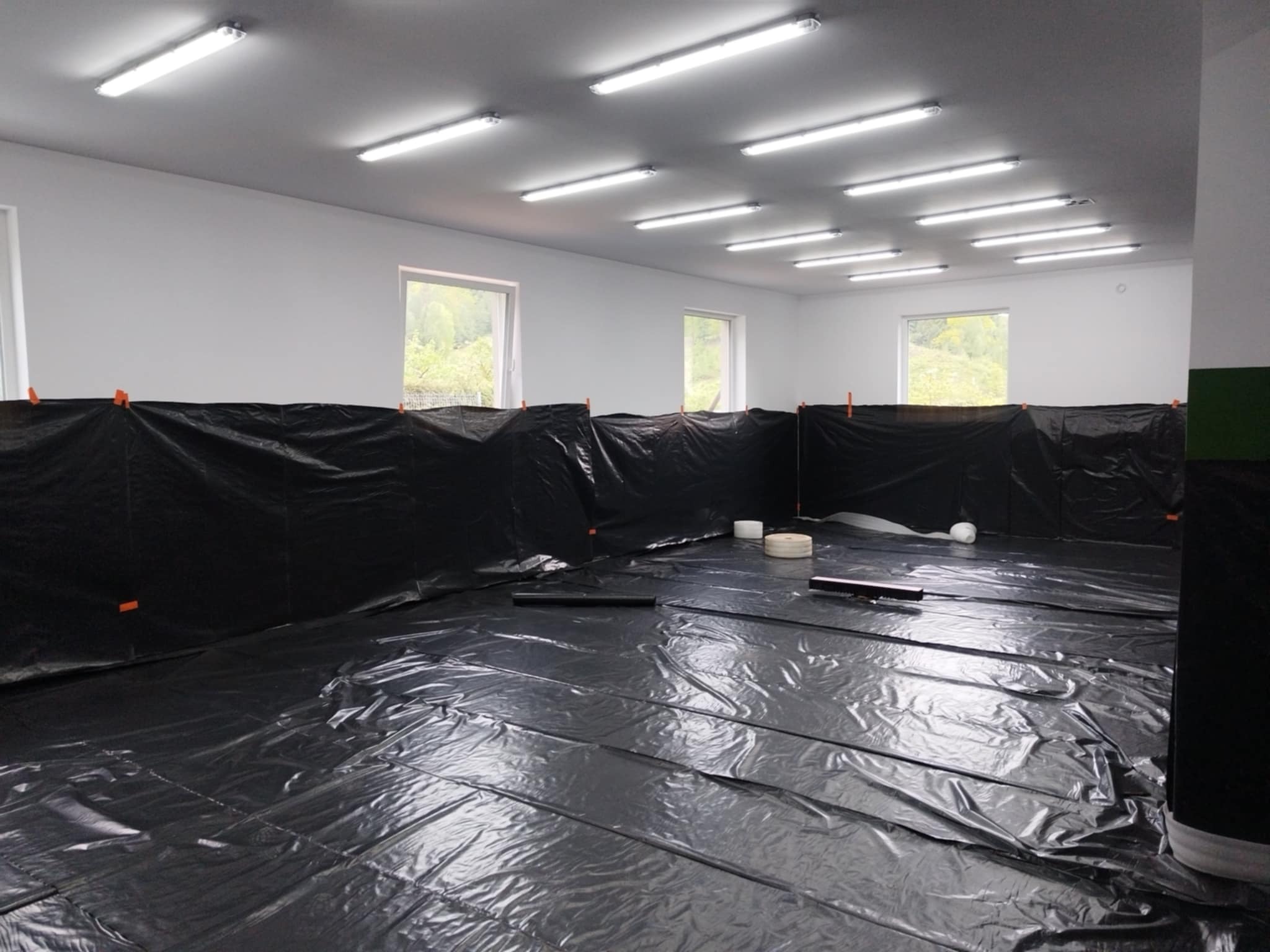 Przygotowanie podłoża pod posadzkę przemysłową: folia ochronna rozłożona na podłodze, zabezpieczone ściany folią, widoczne rolki taśmy i listwy dylatacyjne.