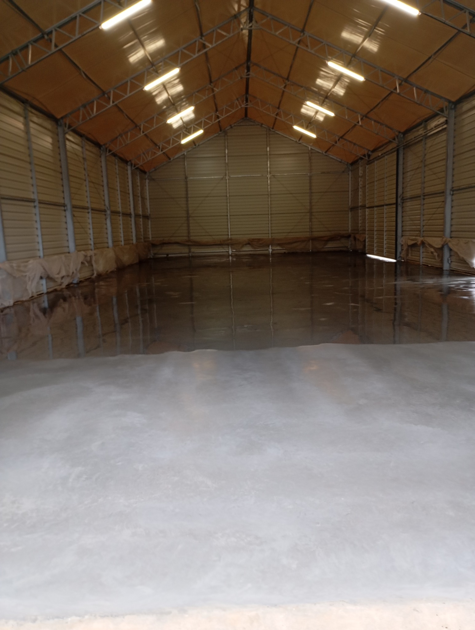 Błyszcząca, świeżo wylana posadzka przemysłowa w hali magazynowej w Kamienniku. Widoczne metalowe ściany i konstrukcja dachu.