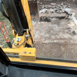 PAT-MAX - Widok z kabiny koparki na gruz i ziemię po rozbiórce, widoczna część ramienia koparki.