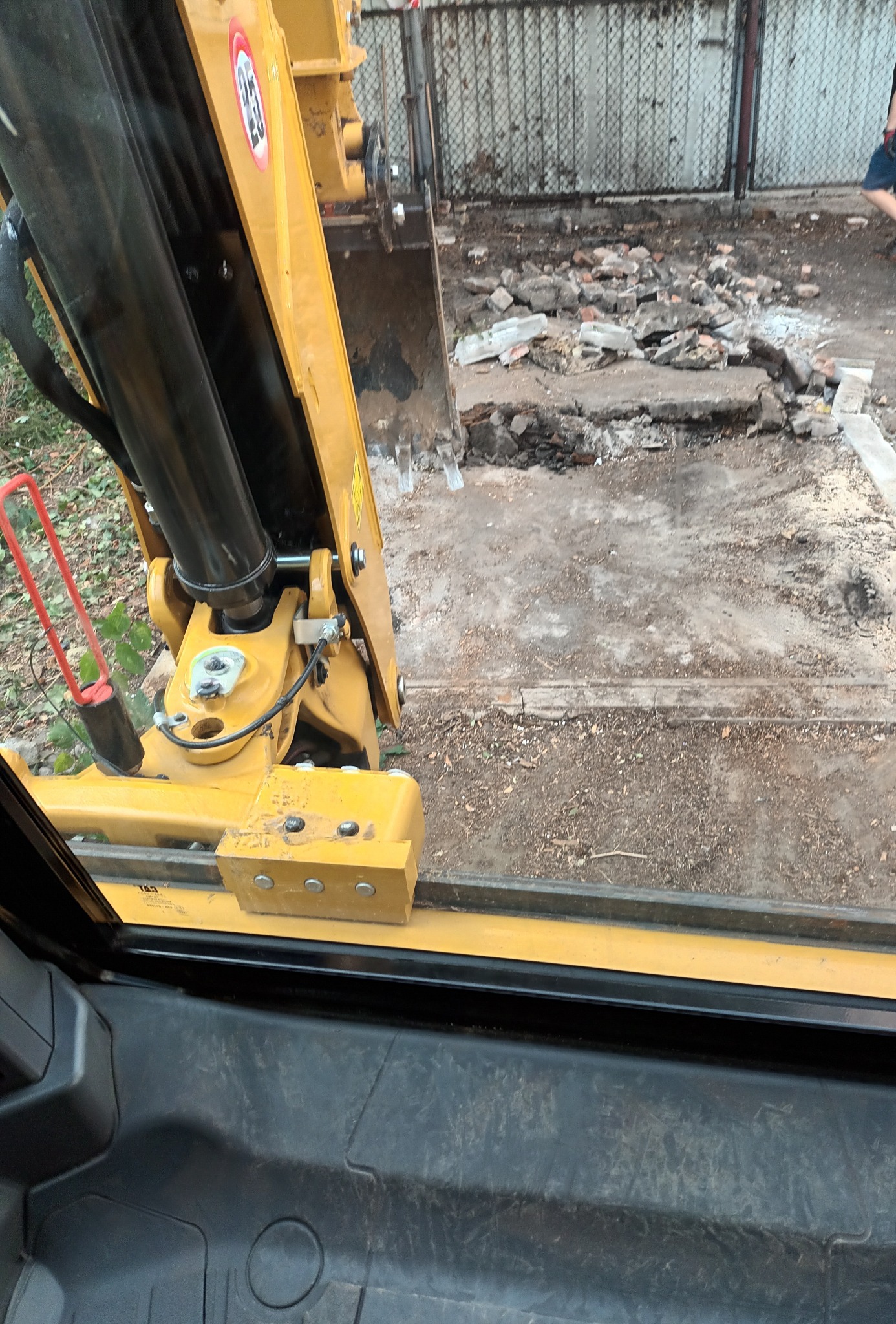 Widok z kabiny koparki na gruz i ziemię po rozbiórce, widoczna część ramienia koparki.