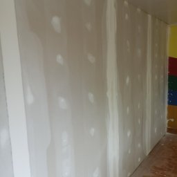 Tomi-BudRem - Ściana w trakcie szpachlowania w pomieszczeniu w Białej Podlaskiej, widoczne świeżo nałożone punkty gładzi na powierzchni płyty gipsowo-kartonowej, przygotowanie do dalszych prac wykończeniowych.