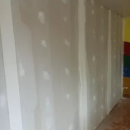 Ściana w trakcie szpachlowania w pomieszczeniu w Białej Podlaskiej, widoczne świeżo nałożone punkty gładzi na powierzchni płyty gipsowo-kartonowej, przygotowanie do dalszych prac wykończeniowych.