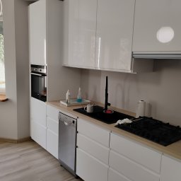 Tomi-BudRem - Nowoczesna kuchnia z białymi, błyszczącymi szafkami, drewnianym blatem, czarnym zlewem z wysoką baterią, płytą gazową i wbudowaną zmywarką Bosch.