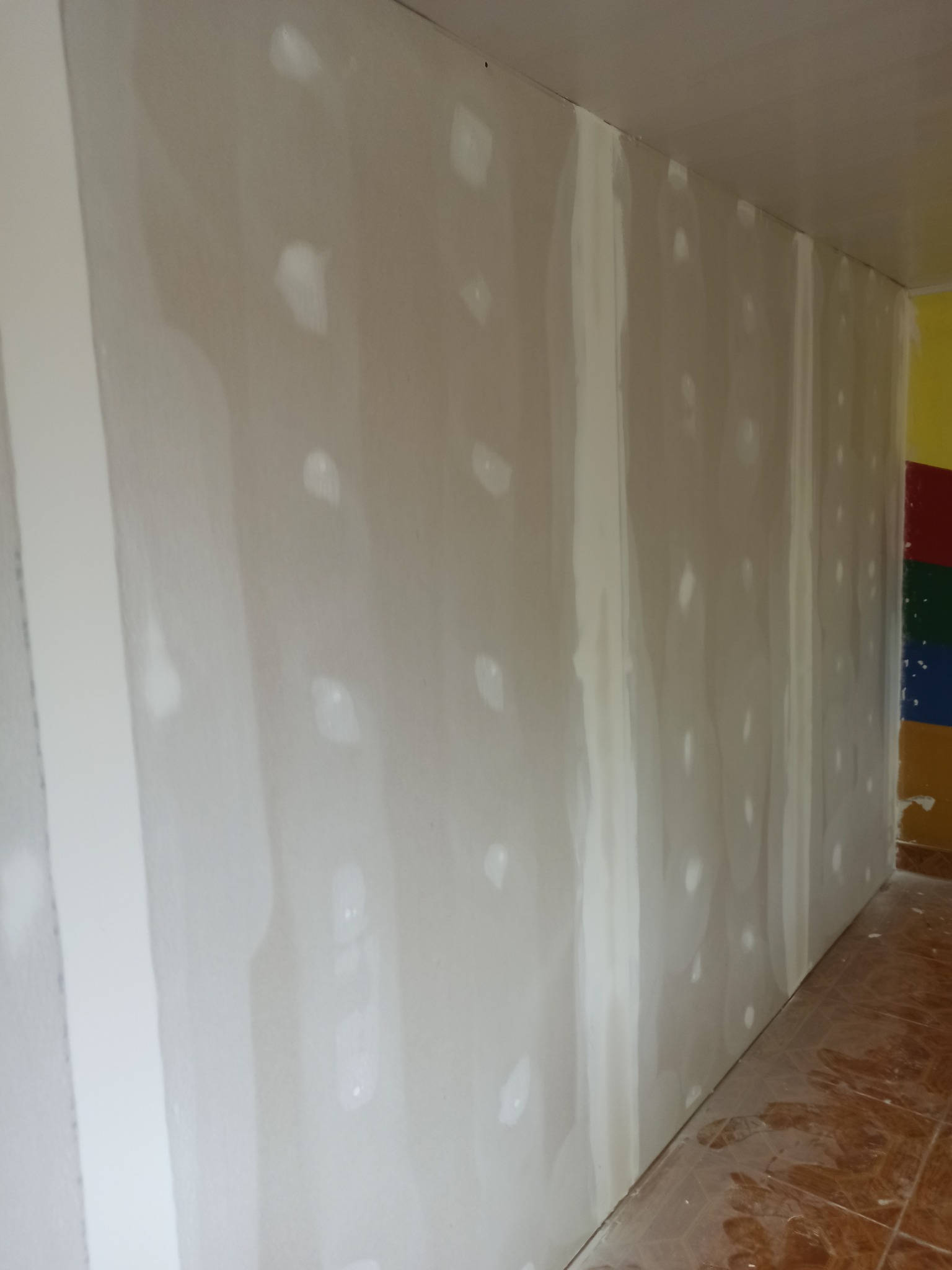 Ściana w trakcie szpachlowania w pomieszczeniu w Białej Podlaskiej, widoczne świeżo nałożone punkty gładzi na powierzchni płyty gipsowo-kartonowej, przygotowanie do dalszych prac wykończeniowych.