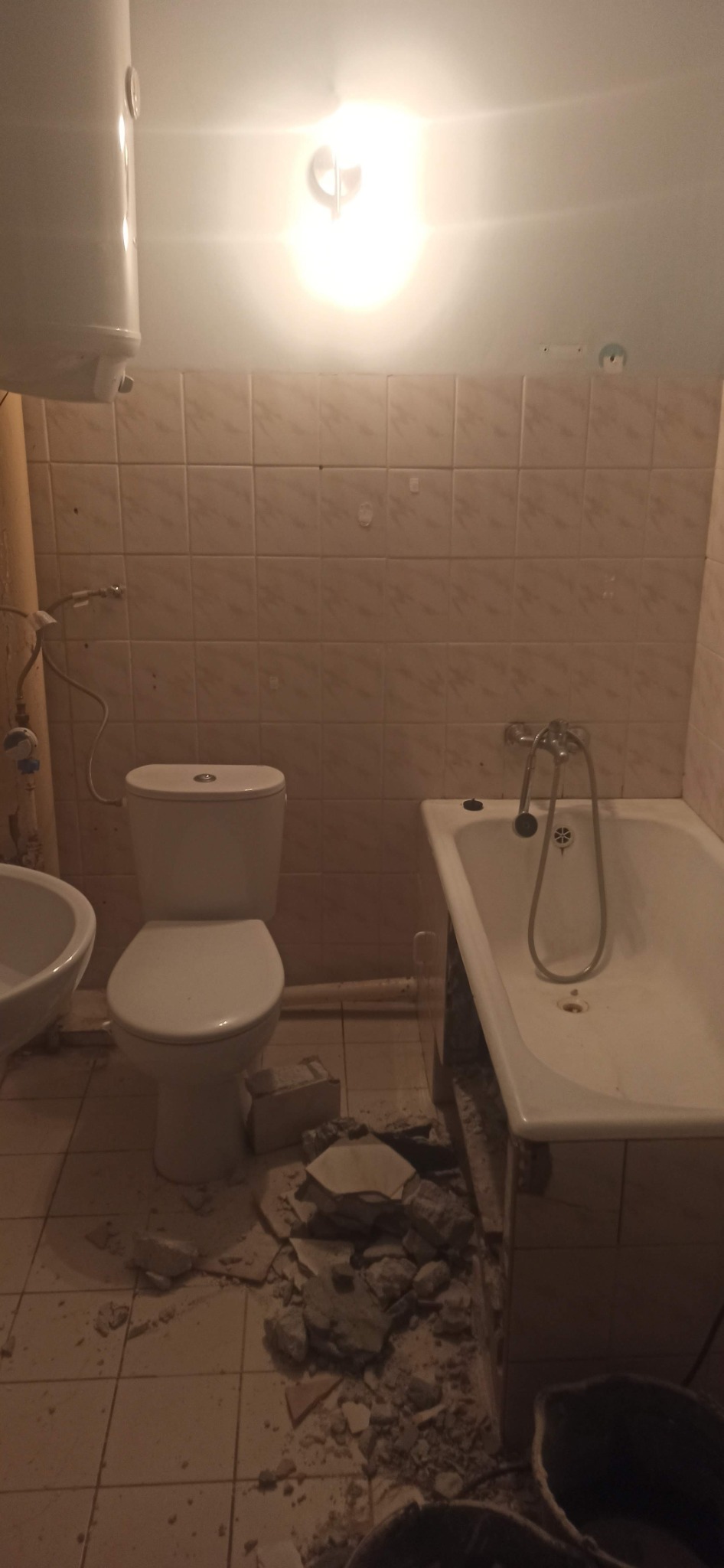 Demontaż płytek w łazience: widok na toaletę, bidet i wannę z usuniętymi fragmentami płytek na podłodze.