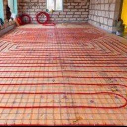 Julian usługi hydrauliczne - Czerwone rury ogrzewania podłogowego ułożone na siatce w surowym stanie, widoczne niedokończone ściany z cegły.